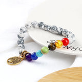 Multicolored beaded bracelet with a gold tree of life charm on a white plate.