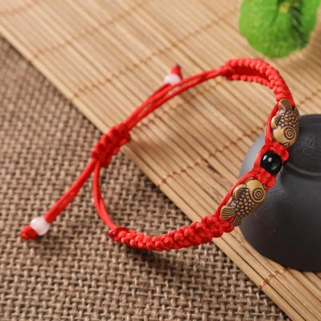Red string bracelet with gold fish-shaped beads on a textured surface