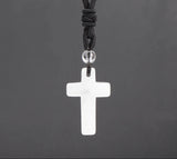 White cross pendant on a black cord against a dark gray background