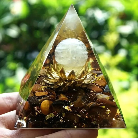 Triangular crystal with a white sphere and gold elements held in a hand against a green blurred background
