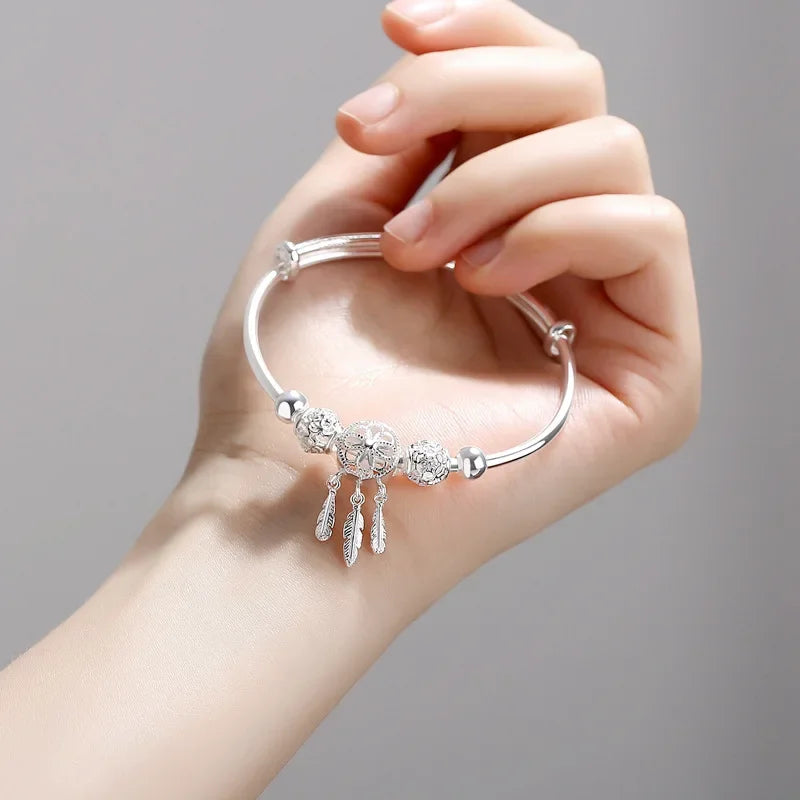 Silver bracelet with charms held by a hand against a gray background