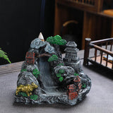 Decorative incense burner shaped like a mountain with buildings and trees on a table.