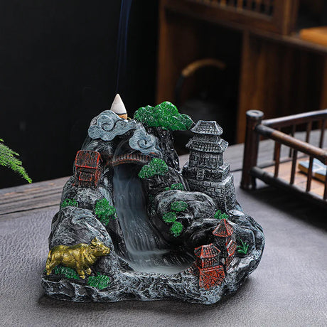 Decorative incense burner shaped like a mountain with buildings and trees on a table.