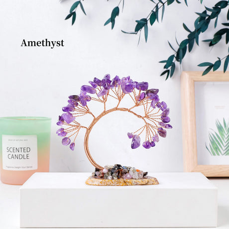 Decorative amethyst tree on a white surface with a candle and framed picture in the background.