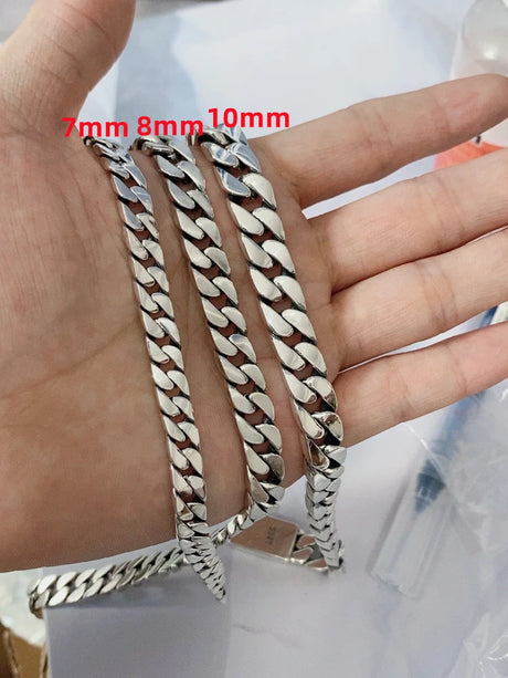 Three silver chain bracelets of different widths held by a hand.
