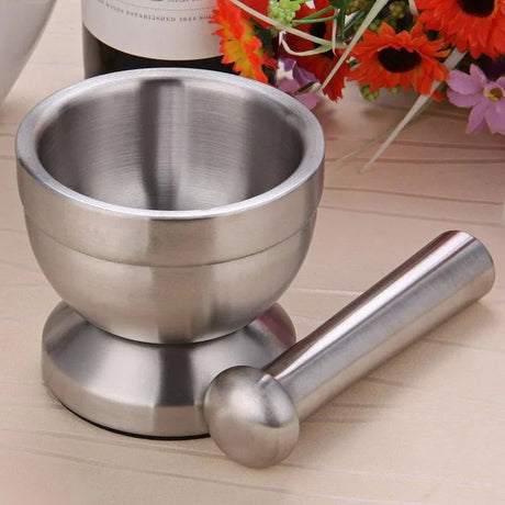 Stainless steel mortar and pestle on a wooden surface with flowers in the background