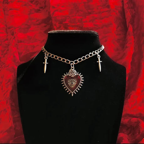 Necklace with heart-shaped pendant and cross charms on a black stand against a red textured background