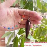 Hand holding a wooden pendulum with colorful beads on a leafy background