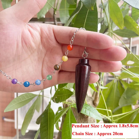 Hand holding a wooden pendulum with colorful beads on a leafy background