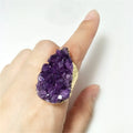 Hand wearing a large purple crystal ring on a white background