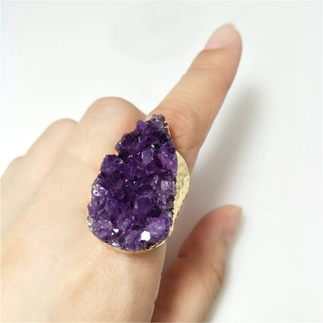 Hand wearing a large purple crystal ring on a white background