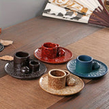 Set of ceramic tea cups and saucers on a wooden table with a fan in the background.