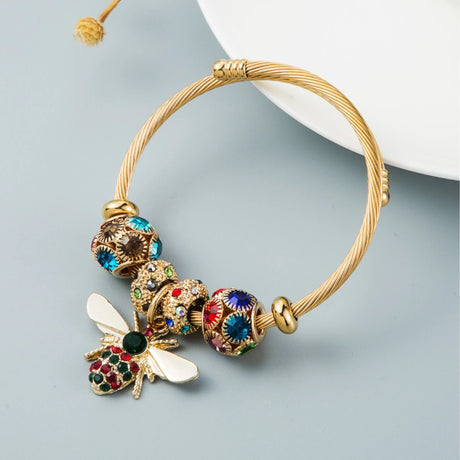 Gold bracelet with colorful beads and a bee charm on a light gray background