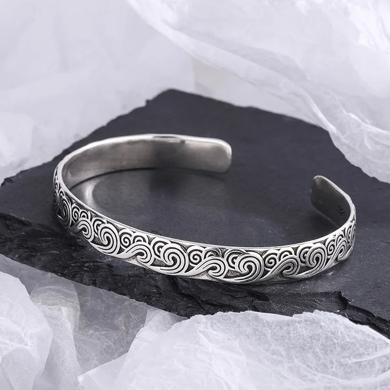Silver bracelet with intricate patterns on a dark stone surface