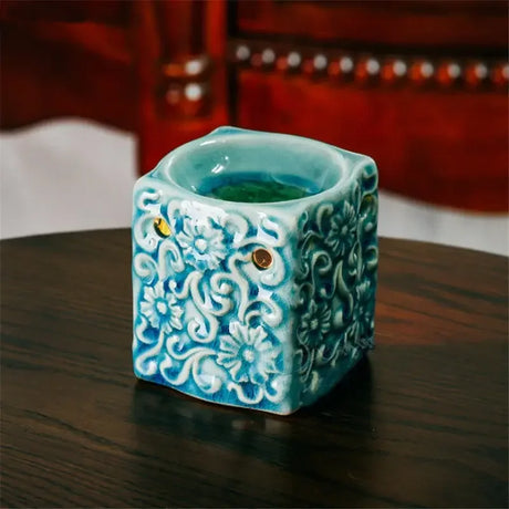Decorative teal ceramic container with floral patterns on a wooden surface.