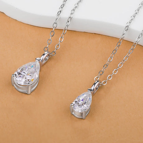Two silver teardrop pendants on chains against a beige background