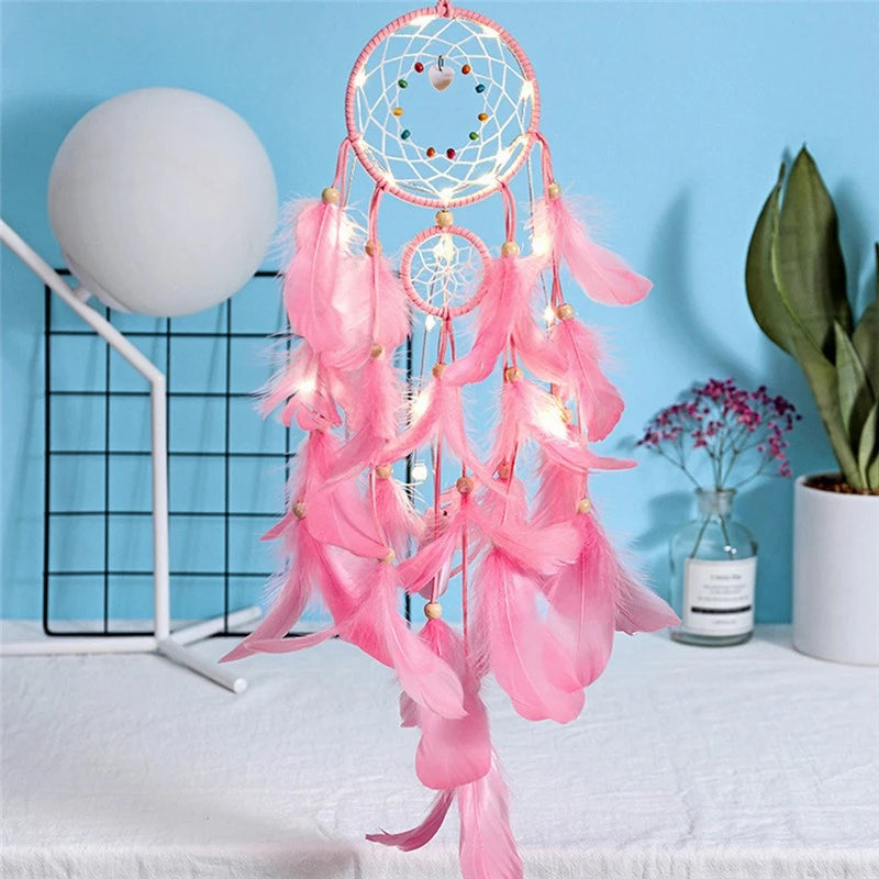 Pink dreamcatcher with feathers on a white surface against a blue wall.