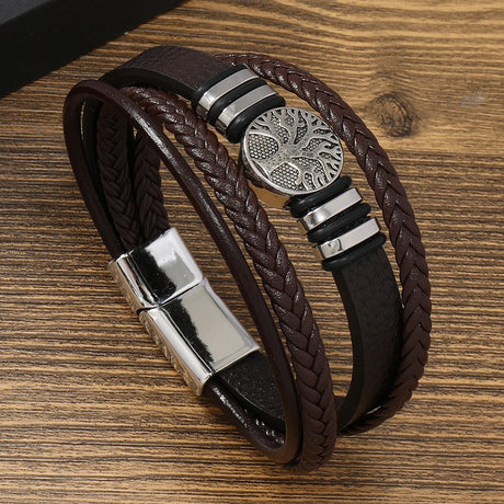 Brown braided leather bracelet with silver metal clasp and tree of life charm on a wooden surface