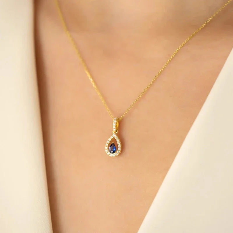 Gold necklace with a teardrop-shaped pendant featuring a blue gemstone on a neutral background