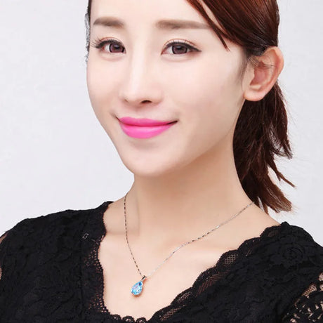 Woman wearing a black lace top and a necklace with a blue pendant on a plain background