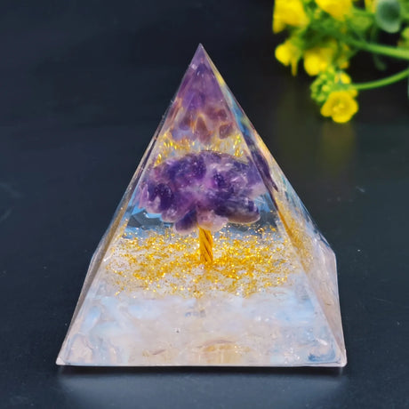 Pyramid-shaped crystal with purple crystal inside on a dark surface with yellow flowers in the background