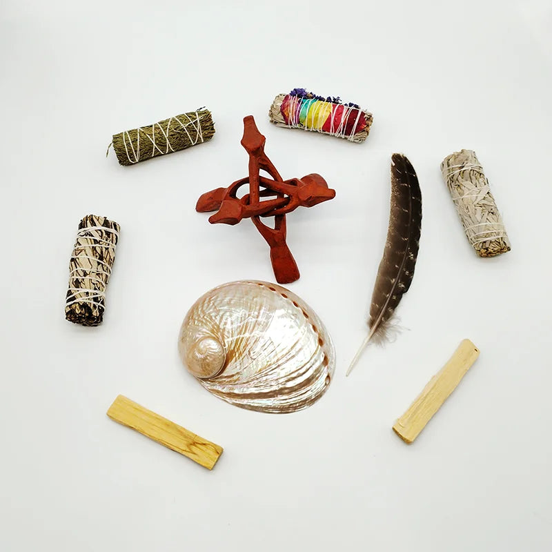 Collection of various items including sage smudge sticks, a shell, a feather, and wooden tools on a white background.