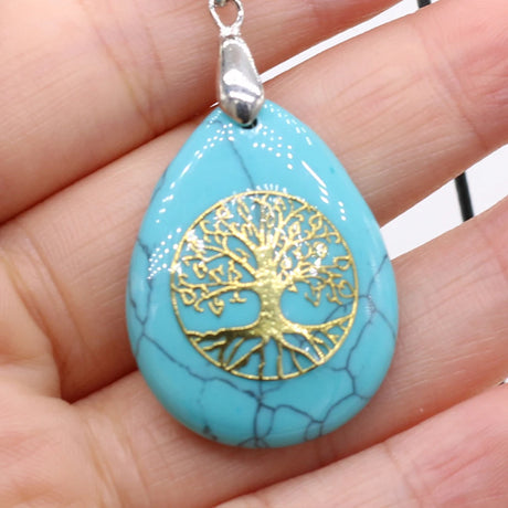 Turquoise teardrop pendant with gold tree design held in a hand