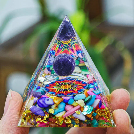 Triangular pyramid with colorful stones and mandala design held by a hand against a blurred natural background