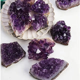 Amethyst crystal clusters on a white surface with a decorative plate.
