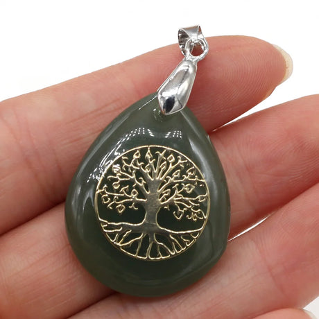Green teardrop pendant with gold tree design held in a hand against a white background