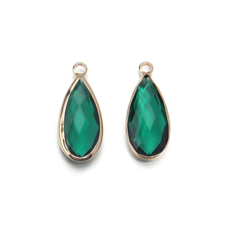 Two green teardrop-shaped earrings with gold settings on a white background