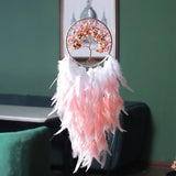 Decorative dreamcatcher with pink feathers against a green wall.