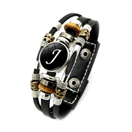 Black leather bracelet with decorative beads and a central black circle with a white letter 'J'.