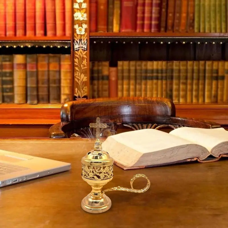 Gold censer on a desk with an open book and laptop in a library setting