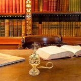 Gold censer on a desk with an open book and laptop in a library setting