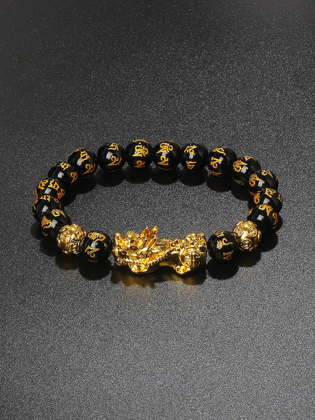 Bracelet with black beads and gold dragon charm on a dark background