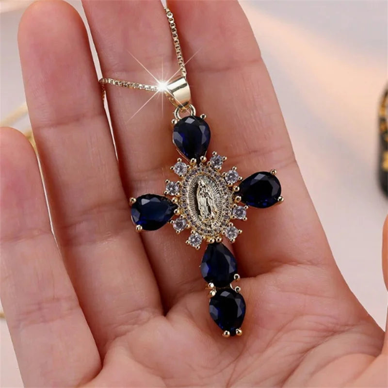 Gold cross pendant with blue stones held in a hand against a neutral background
