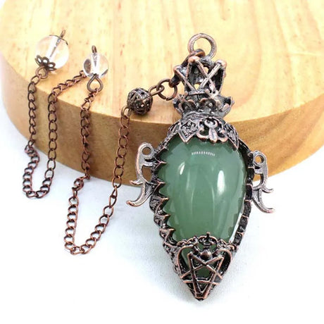 Green teardrop pendant with intricate metalwork on a wooden surface