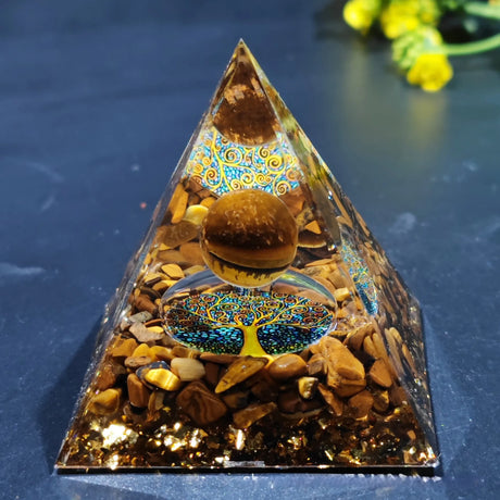 Pyramid-shaped decorative item with stones and a tree of life design on a dark surface.