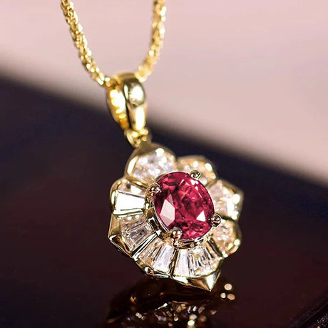 Gold pendant with a red gemstone and diamond accents on a reflective surface.