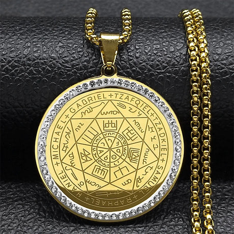 Gold pendant with intricate design and chain on a textured black surface