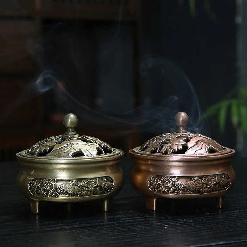 Two ornate bronze incense burners with smoke rising from them on a dark surface.