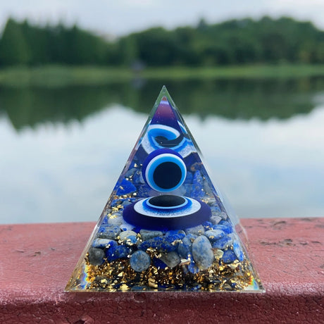 Pyramid-shaped crystal with blue and gold elements on a red surface with a blurred natural background