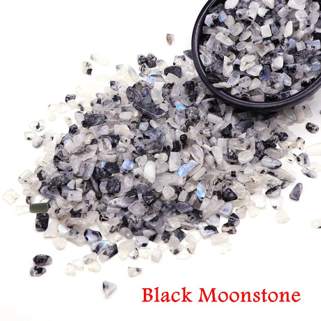 Black moonstone stones with a small bowl filled with them on a white background.