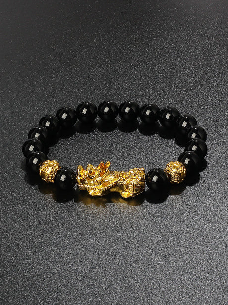 Black beaded bracelet with gold dragon charm on a dark background