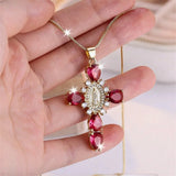 Gold necklace with red gemstones held in a hand against a blurred background
