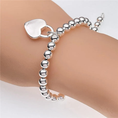 Silver beaded bracelet with a heart charm on a wrist against a white background