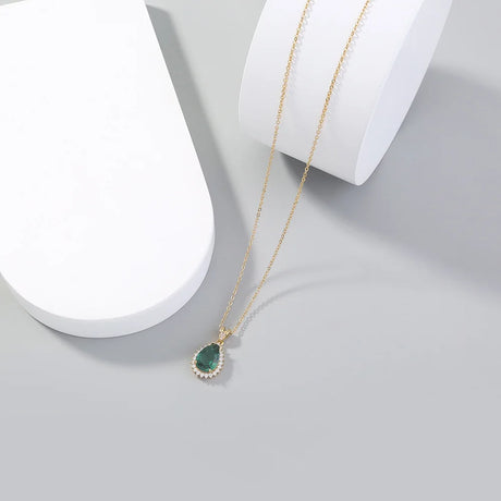 Gold necklace with a green pendant on a white surface