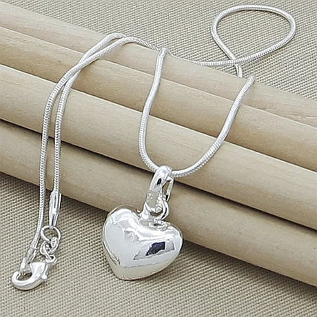 Silver heart-shaped pendant necklace on a beige surface