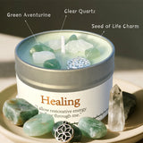 Candle in a tin labeled 'Healing' with stones and crystals around it.